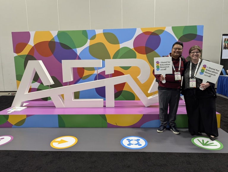 Two graduate students are standing next to a large AERA sign
