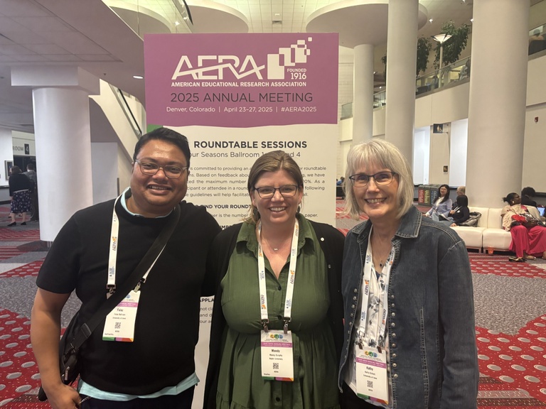 Two students and a faculty member stand in front of an AERA sign